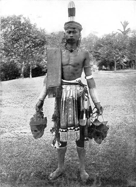 Fotografia feita por Charles Hose, entre 1900 e 1912, mostra homem Dayak com trajes t picos da tribo, segurando dois cr nios nas m os  
