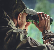 Caucasian Hunter in Masking Camouflage Uniform with Binoculars  Hunter Spotting Game  Poacher or Soldier Clothing 